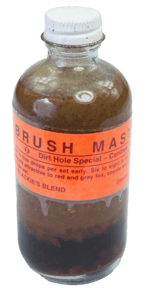 A small glass bottle labeled "Blackie's Brush Master Lure" is filled with brown liquid and sealed with a metal cap.