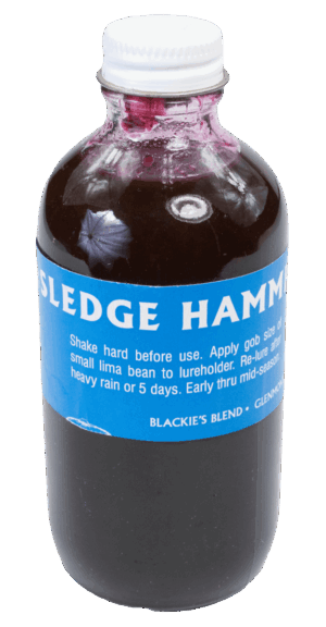 A bottle of Blackie's Sledge Hammer Lure with dark liquid and a blue label featuring coon food lure instructions.